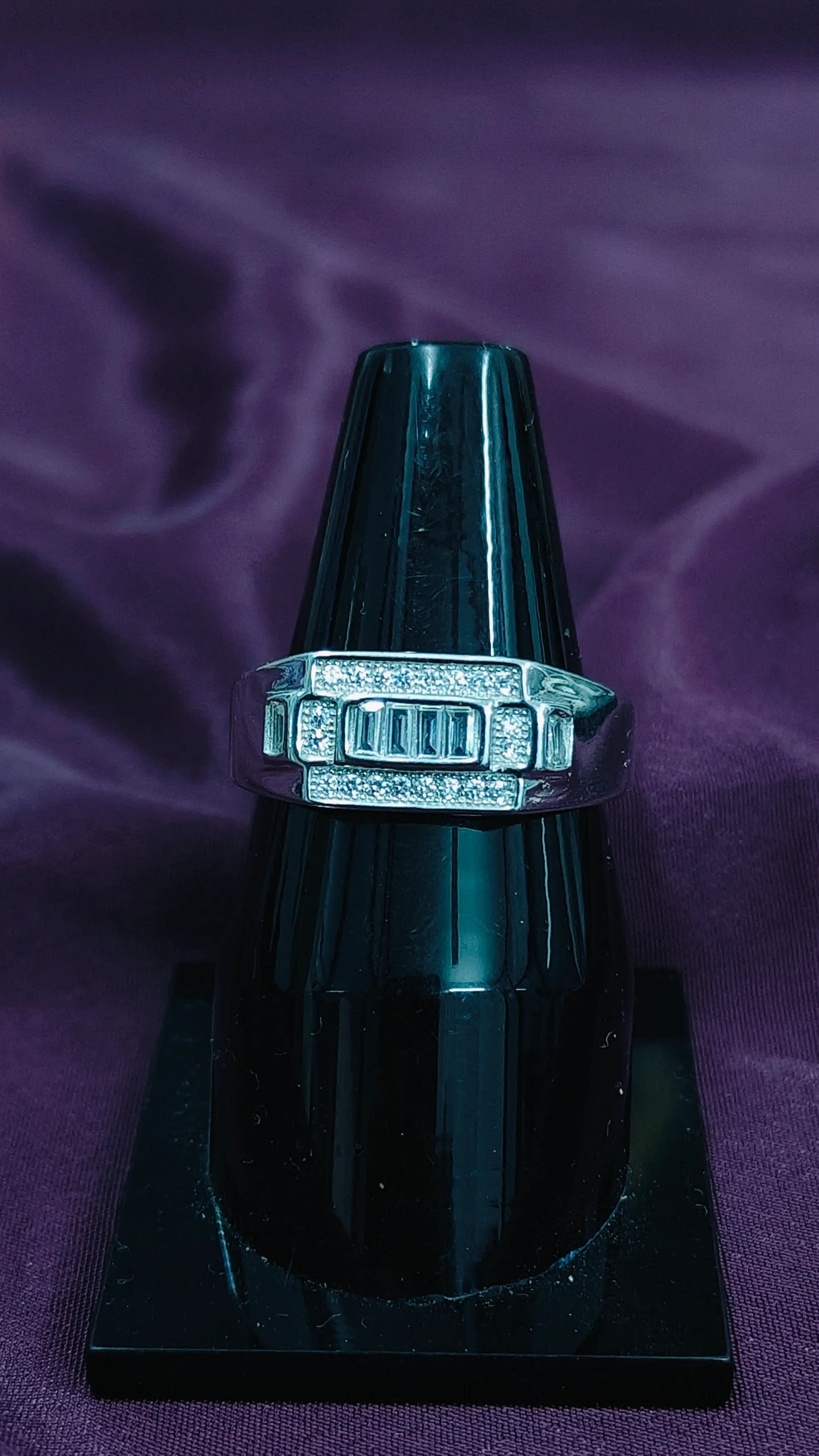 Silver ring with gemstones on a black stand against a purple fabric background
